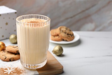 Glass of delicious eggnog with cinnamon on white table, space for text
