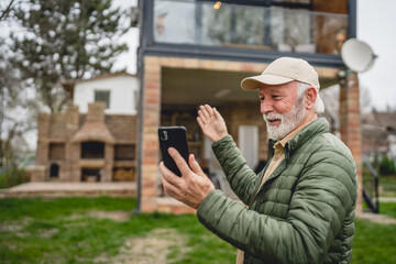 One senior man stand in front of tiny house in day use smart phone