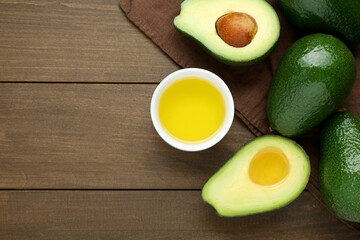 Bowl with oil and ripe fresh avocados on wooden table, flat lay. Space for text