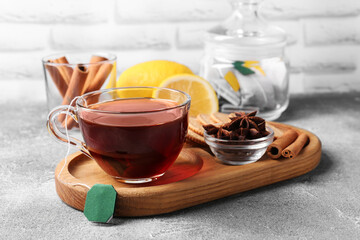 Tea bag in glass cup, anise stars and cinnamon sticks on light grey table