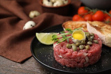 Tasty beef steak tartare served with quail egg and other accompaniments on wooden table, closeup