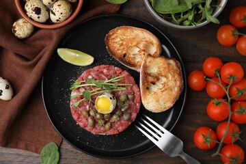 Tasty beef steak tartare served with quail egg and other accompaniments on wooden table, flat lay