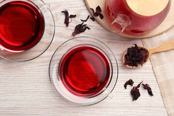 Cup of fresh hibiscus tea and dry flower leaves on wooden table, flat lay