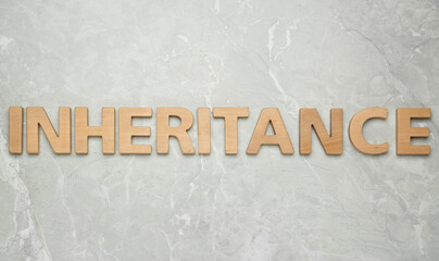 Word Inheritance made with wooden letters on light marble background, flat lay