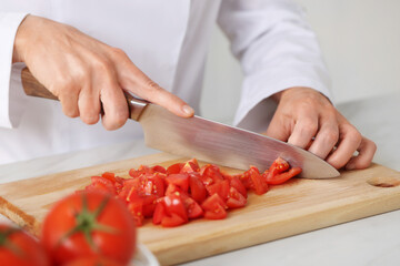 Professional chef cutting tomatoes at white marble table indoors, closeup