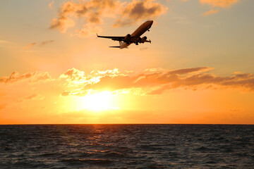 Naklejka na ściany i meble Plane flying over sea during sunset. Sun shining through clouds