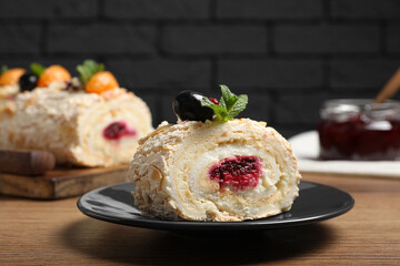 Slice of tasty meringue roll with jam, tangerine slices and mint leaves on wooden table