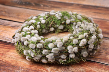 Wreath made of beautiful willow flowers on wooden table, closeup