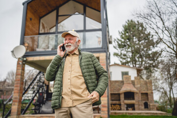 One senior man stand in front of tiny house in day use smart phone