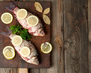 Fototapeta na wymiar fresh crucian fish sprinkled with spices and lemon slices and lies on a brown wooden cutting board