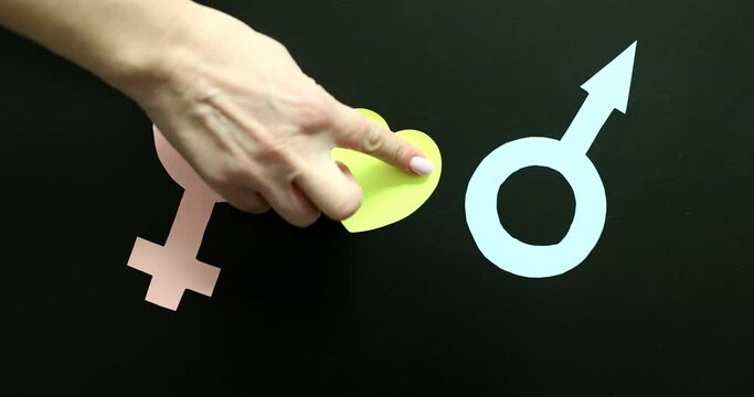 Hand putting paper heart between female and male icon on black background 4k movie slow motion. Natural love between man and woman concept