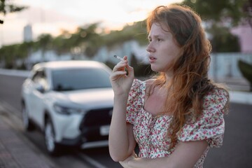 young girl smokes next a broken car and thinks what to do next, the concept of a problem on the road, girl driver