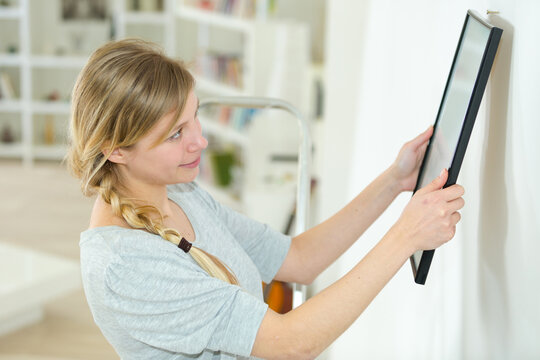 woman putting photo frame on white wall