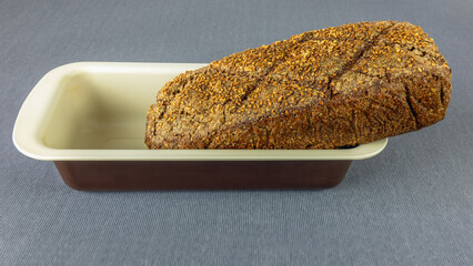 A loaf of dark bread in a baking dish on a tablecloth
