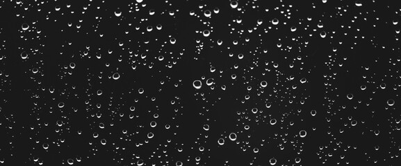 Atmospheric minimal grayscale backdrop with rain droplets on glass. Wet window with rainy drops and dirt spots closeup. Blurry minimalist monochrome background of dirty window glass with raindrops.