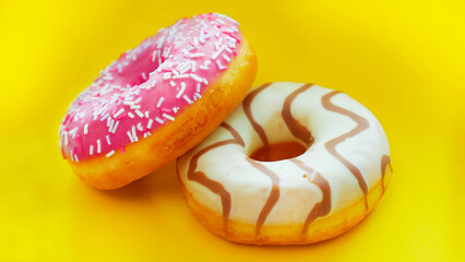 Two donuts with icing on a bright yellow background