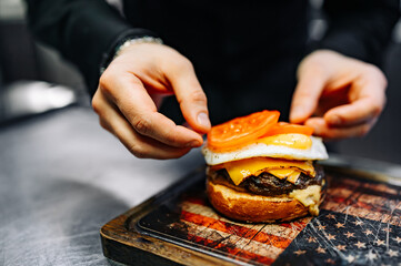 chef hand cooking cheeseburger with vegetables and egg on restaurant kitchen