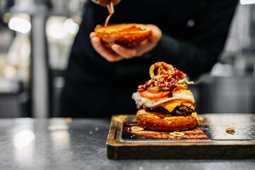 chef hand cooking cheeseburger with vegetables and egg on restaurant kitchen