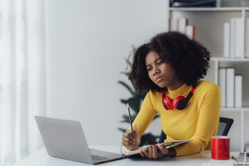 Beautiful American women student studying online takes notes on her laptop to gather information about her work smiling face and a happy study posture.