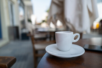 There is a white espresso cup on a table in a restaurant in the pedestrian zone.
