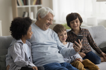 Cheerful grandpa and diverse little grandsons talking on video conference call on smartphones,...