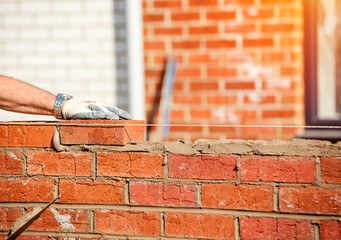 Hard working bricklayer lays bricks on cement mix on construction site. Fight housing crisis by...