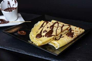 Homemade crepes with hot dark chocolate on a black background