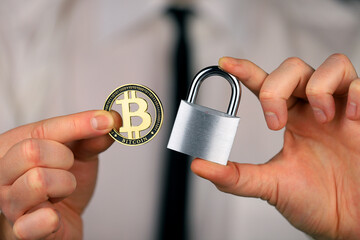 A businessman holds a silver padlock and physical version of bitcoin in his hands. Prohibition of cryptocurrencies, regulations, restrictions or security, protection, privacy.