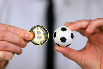 A businessman in a white shirt and black tie holding football and bitcoin in his hands.