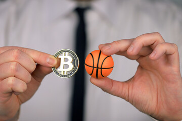 A businessman in a white shirt and black tie holding basketball ball and bitcoin in his hands.