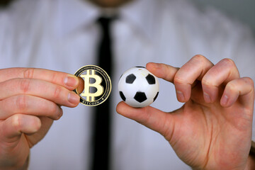 A businessman in a white shirt and black tie holding football and bitcoin in his hands.