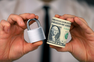 Businessman holding a silver padlock and bundle of dollars in his hand. Money security.