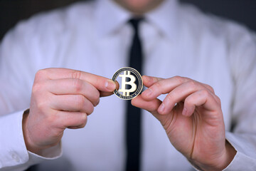 A businessman in a white shirt and black tie holds a physical version of bitcoin in his hands.
