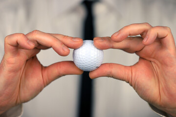 A businessman in a white shirt and black tie holding golf ball in his hands.