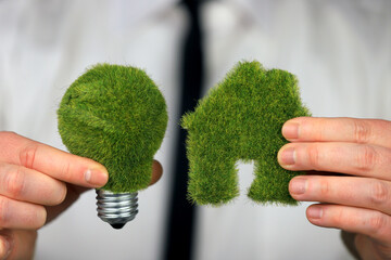 Businessman holding green eco light bulb with grass and miniature house. Renewable energy concept. Electricity prices, energy saving in the household.