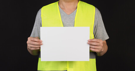 The man wears Safety Vest and holding A4 paper on black background.
