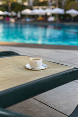 A cup of coffee on the sunbed in the swimming pool area outdoor. Relaxation, vacation concept