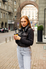 Young woman in black jacket and jeans with coffee on the street urban fashion