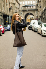 Young woman in black jacket and jeans with coffee on the street urban fashion