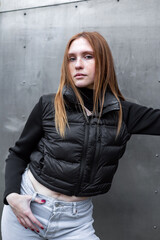 Young woman in black jacket and jeans posing near steel wall. Fashion cold tone