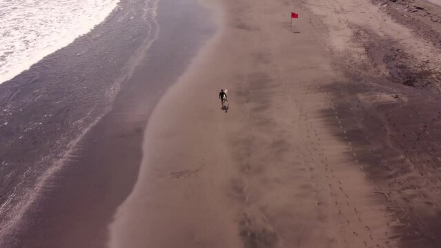 Video aéreo 4K, de surfista con la tabla de surf, caminando por la arena en una playa.