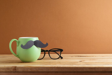 Happy Father's day concept with green coffee cup, mustache and eyeglasses on wooden table over brown background