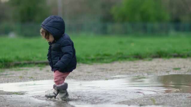 Little child walk through puddle. Toddler jumping in puddle and splashing water. Having fun at rainy weather. 