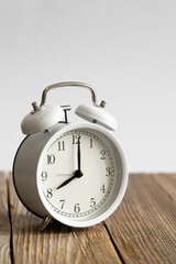 White alarm clock on a wooden surface close-up, blurred white background, space for text, concept of morning, deadline, time management.