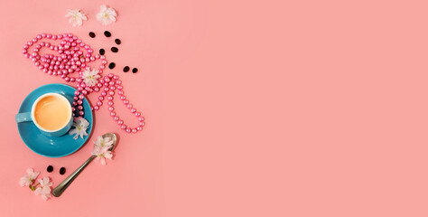 blue coffee cup with espresso. neclace of pearls, flower and coffee beans over pink background with copy space like romantic female concept 