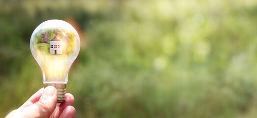 Concept image of a light bulb and small house in nature. Idea of ecology, solar energy, and...