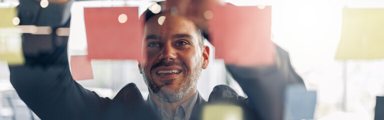 Close up of smiling businessman is glues sticky notes on motivation board in modern office