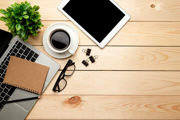 Top view office table desk. Workspace with blank, office supplies,Laptop, pencil, green leaf, and coffee cup on wood background.