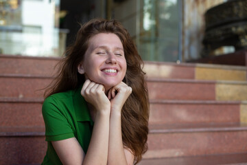 young beautiful woman is sitting on steps near hotel or new house, home and smiling