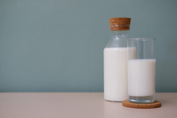 A glass of milk and bottle of milk on wooden table in green background.